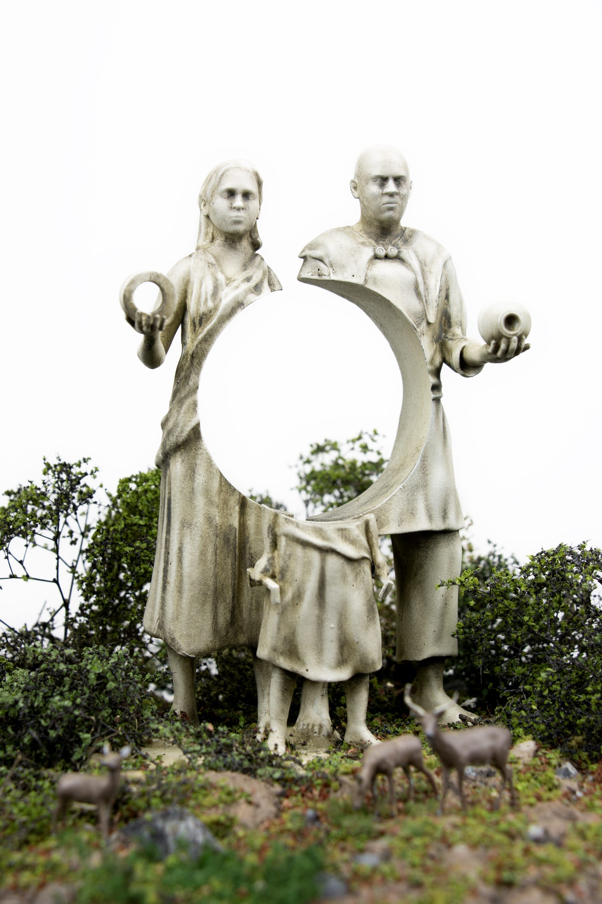 a miniature person looking at three figurative statues with circular cutouts
