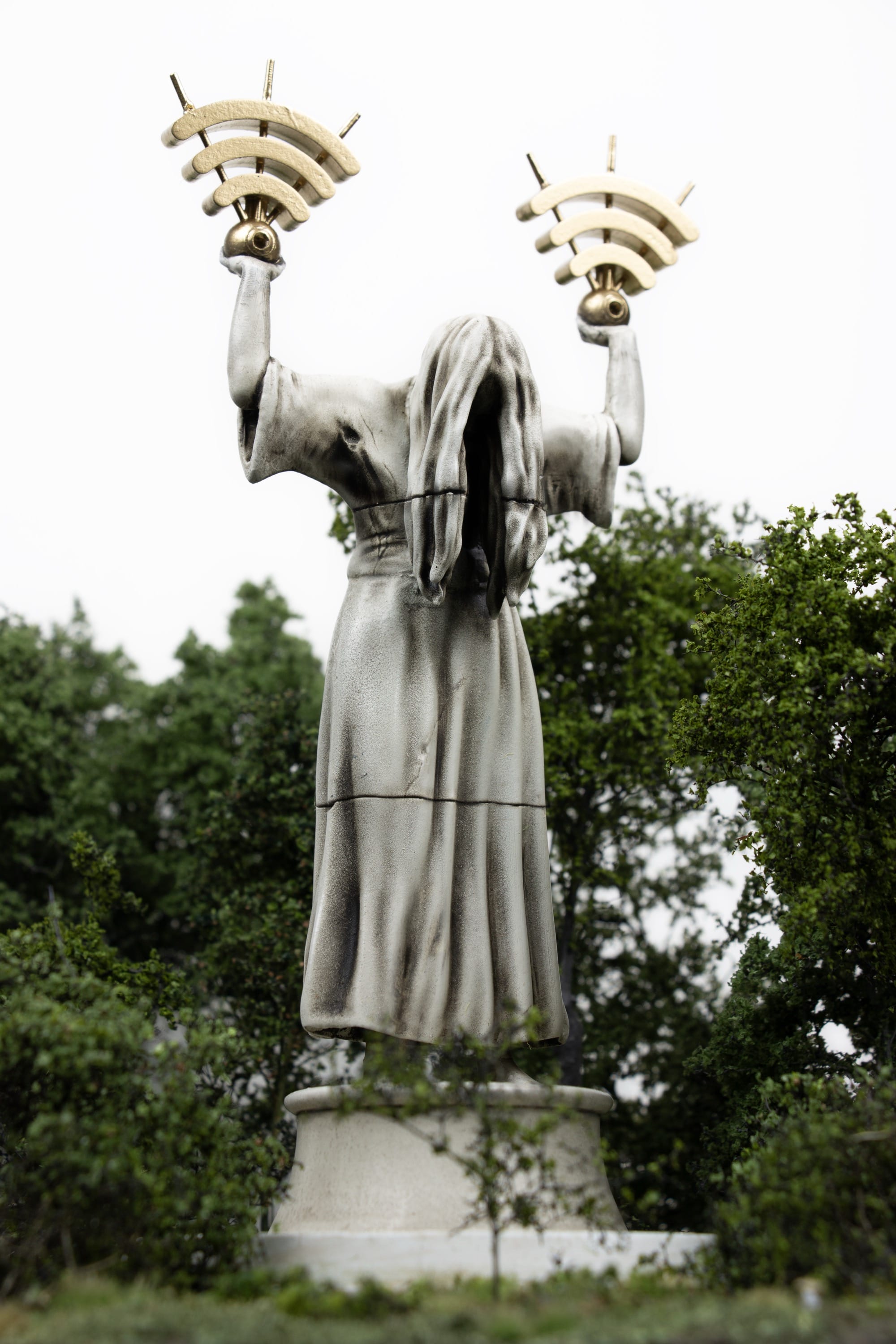 a large statue with long hair covering her face holds two wifi symbols in her hands while a small figure looks up from below