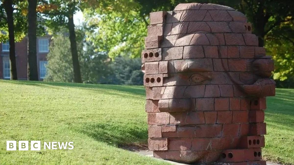 A brick-built statue depicting the head of Josiah Wedgwood in a stylised fashion. It is positioned on a grass verge.