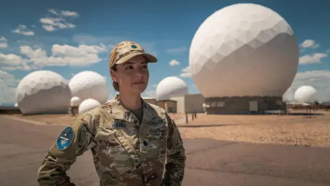 BBC/Matthew Goddard Lt Col Ann Hughes standing in front of a giant radar array in Colorado