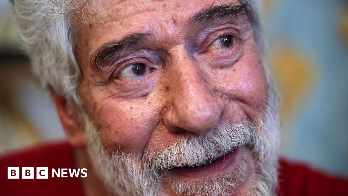 Georges Abdallah, a grey-haired 74-year-old with grey moustache and beard, sits in his prison cell in a red shirt