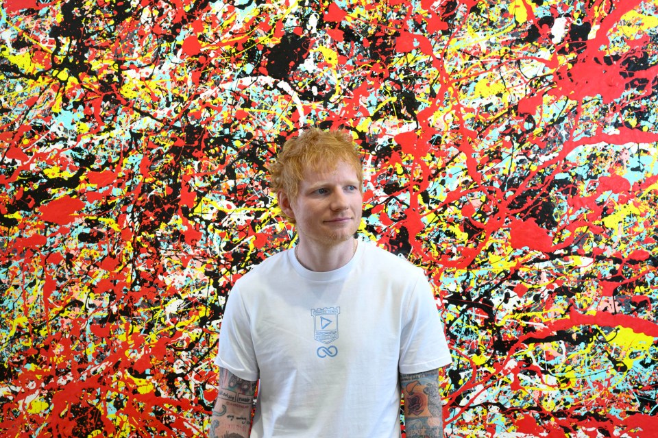 Ed Sheeran standing in front of one of his paintings.