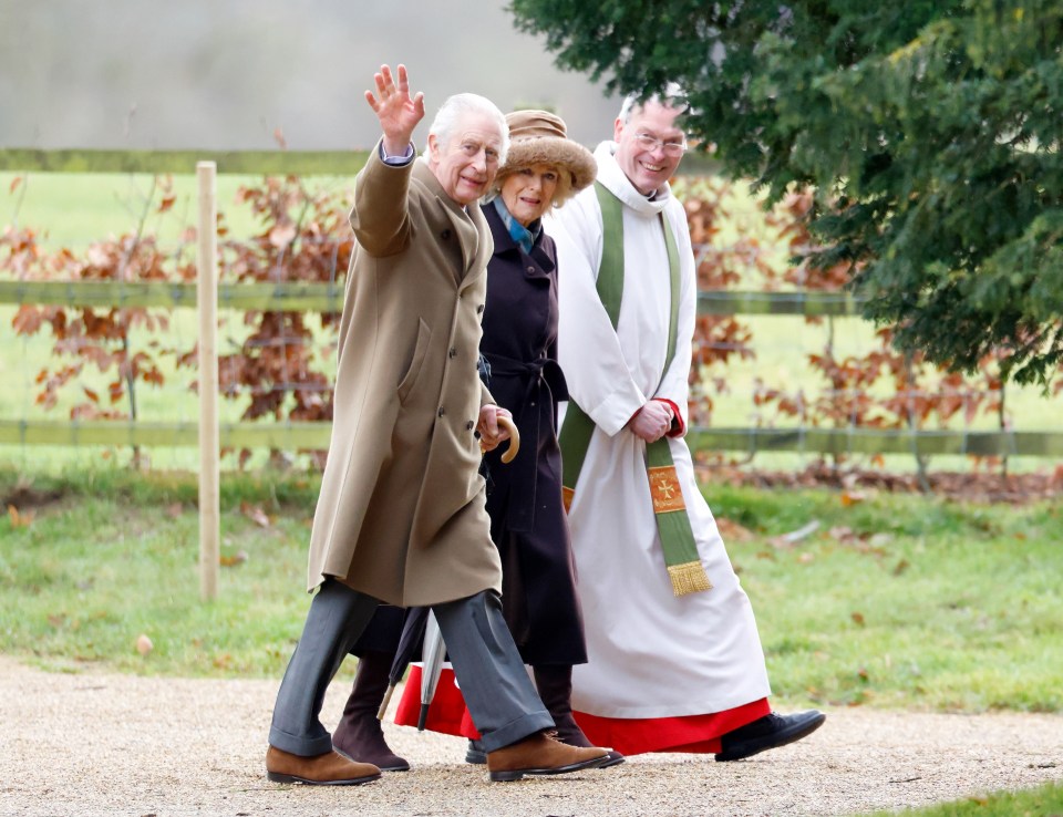 King Charles III, Queen Camilla, and a reverend walking and waving.