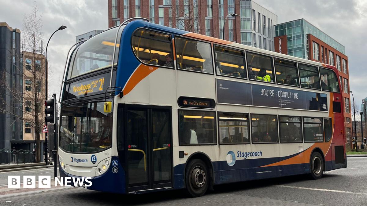 A red, blue and white double decker bus drives past a multi-storey building.