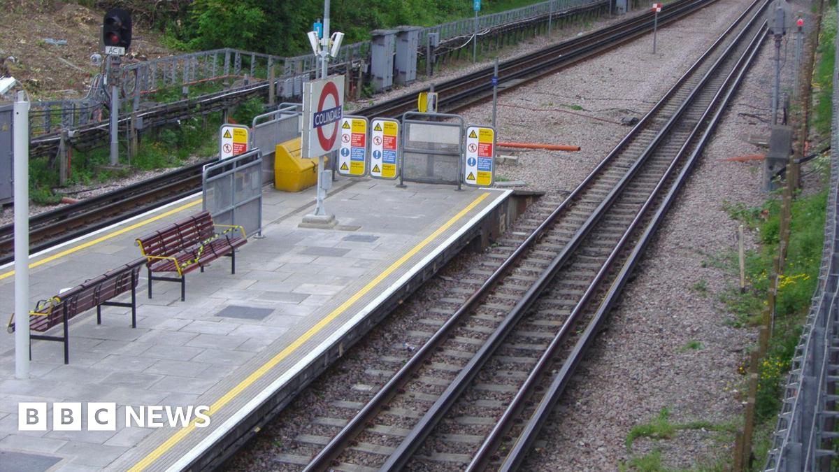 Colindale station platform as seen from above shows Tube roundel, wooden benches and train tracks