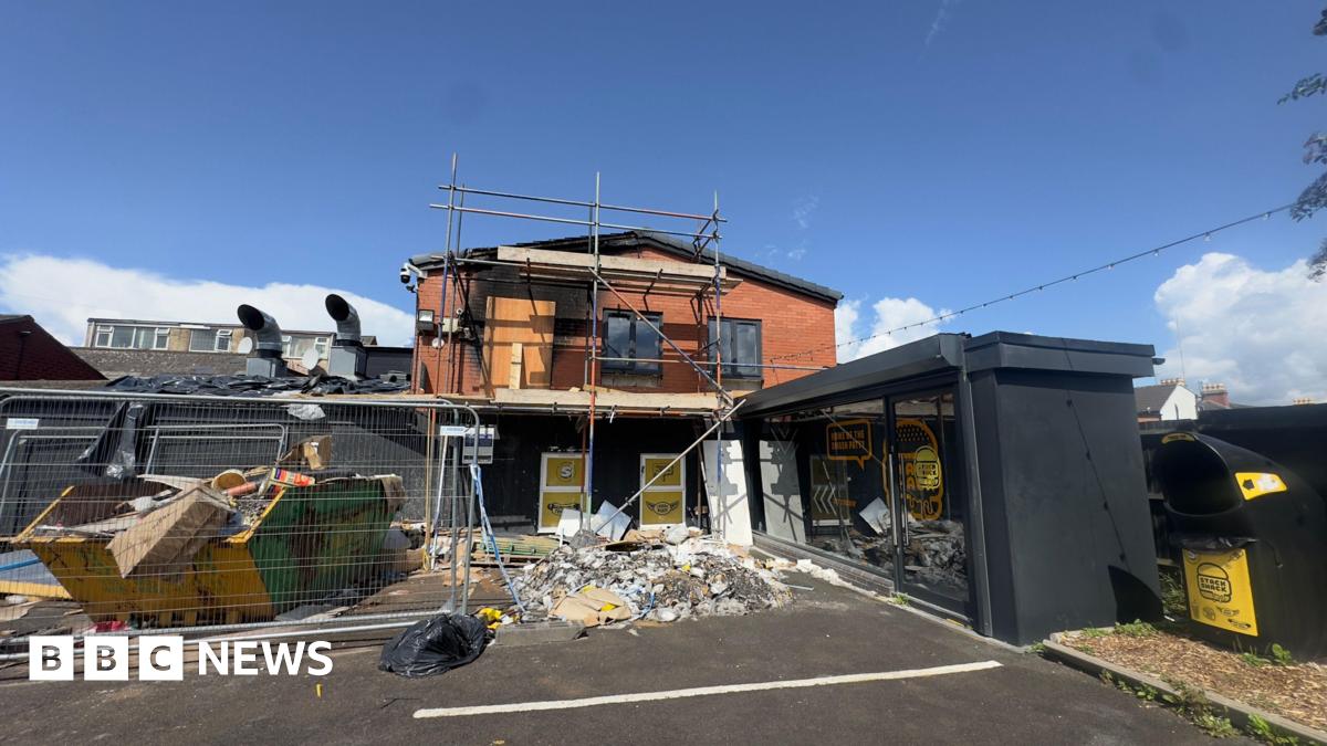 A restaurant destroyed by an arson attack. A small two storey-building is seen with rubble piled in front of it, black staining on the red bricks from the smoke and scaffolding up against the building. A skip is also outside the premises piled with rubbish.