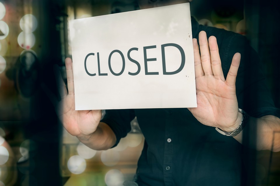 Person holding a "Closed" sign in a shop window.