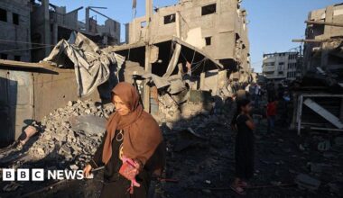 A Palestinian woman walks past damaged buildings after an Israeli strike on the Bureij refugee camp in the central Gaza Strip. Photo: 23 July 2025