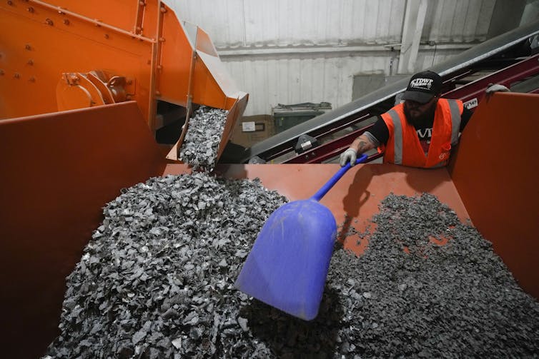 A person uses a shovel to reach into a large bin of crushed material.