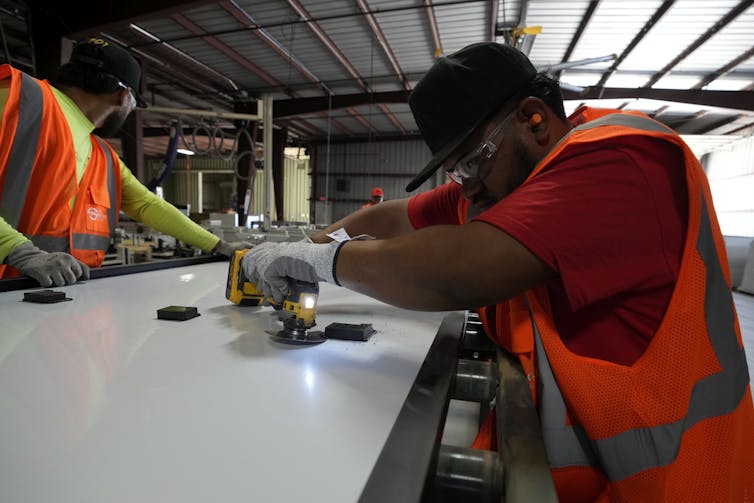 People in reflective vests and protective clothing use tools to take apart a large item.