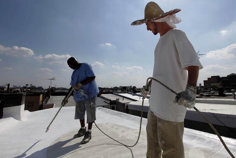 Two workers apply paint to a flat roof.