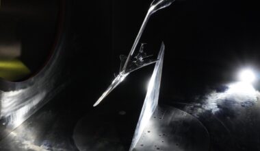a long, narrow, silver model of an aircraft hangs from a boom in a dark concrete tunnel