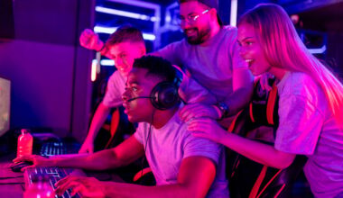 People standing near a gamer on a computer and cheering.