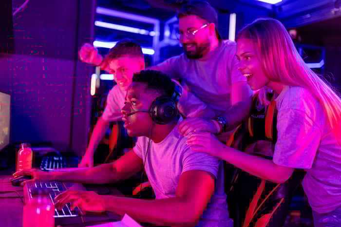 People standing near a gamer on a computer and cheering.