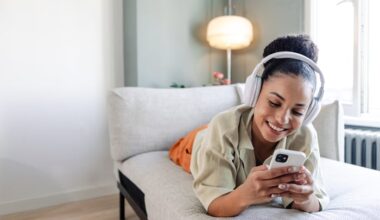 Happy person using headphones and a phone while lying on a couch.