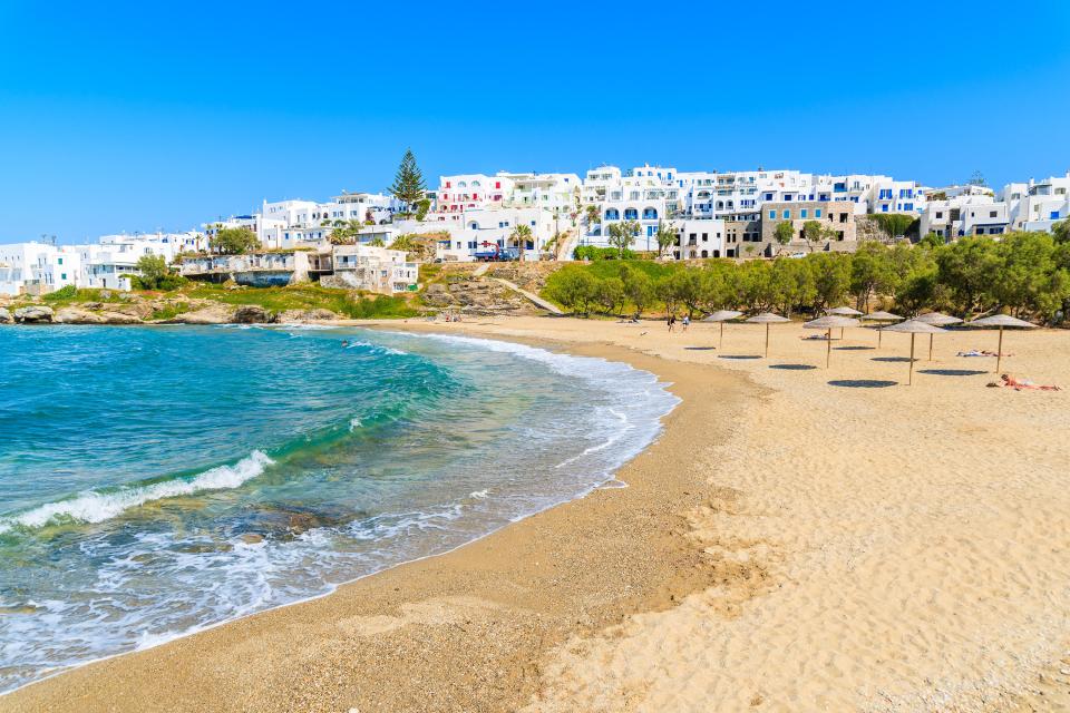 Sandy beach with turquoise water and whitewashed buildings in Naoussa, Paros, Greece.