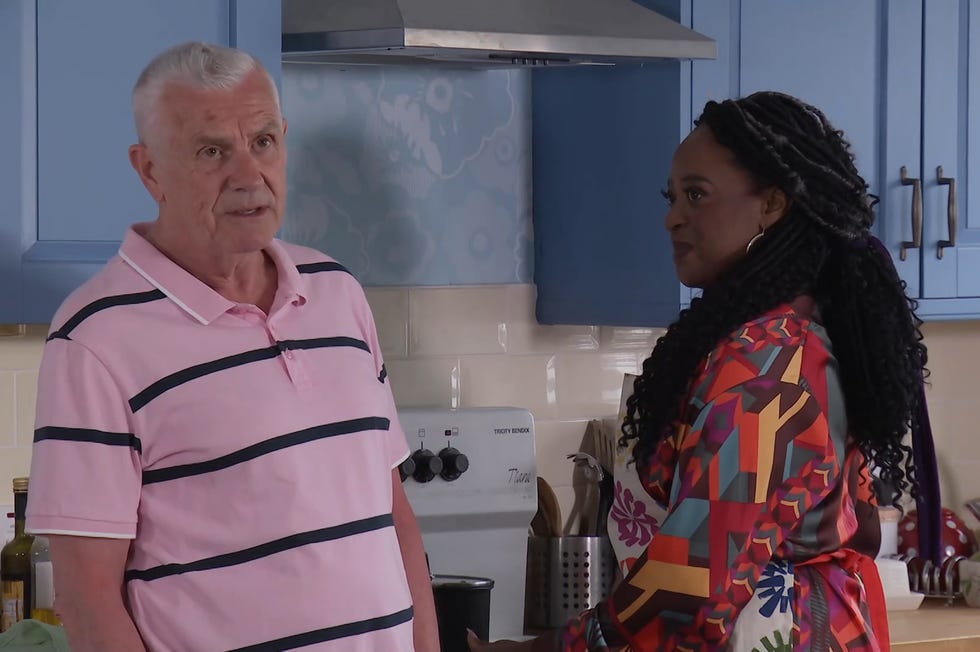 hollyoaks, jack osborne in a pink t shirt in the kitchen next to pearl, wearing a multicoloured outfit with an apron