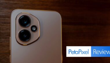 Close-up of a smartphone's rear camera module with two large lenses and a small sensor, placed on a wooden surface. The Petapixel Reviews logo appears in the bottom right corner.