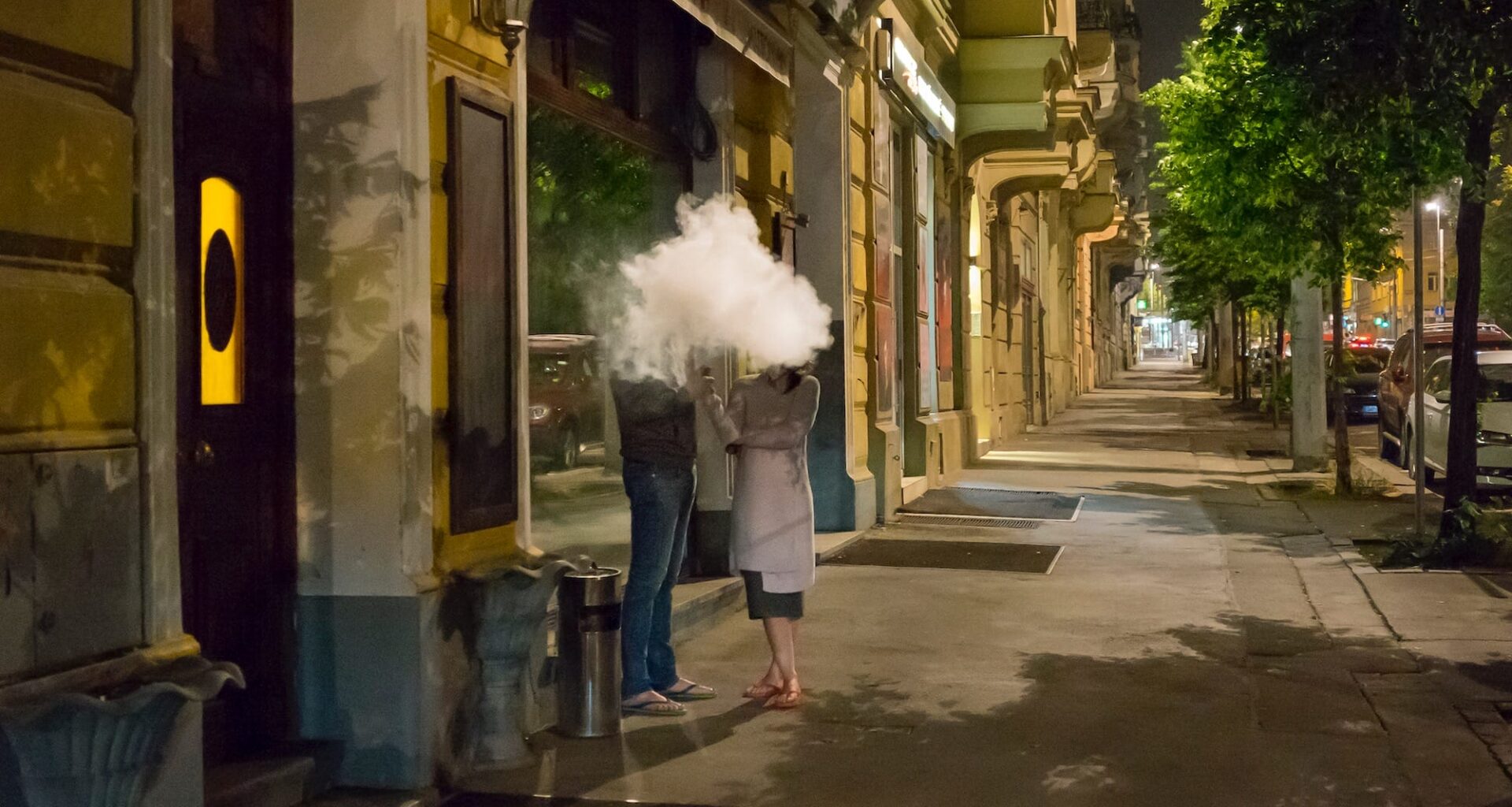 a photograph of two people standing outside on a street in a cloud of smoke