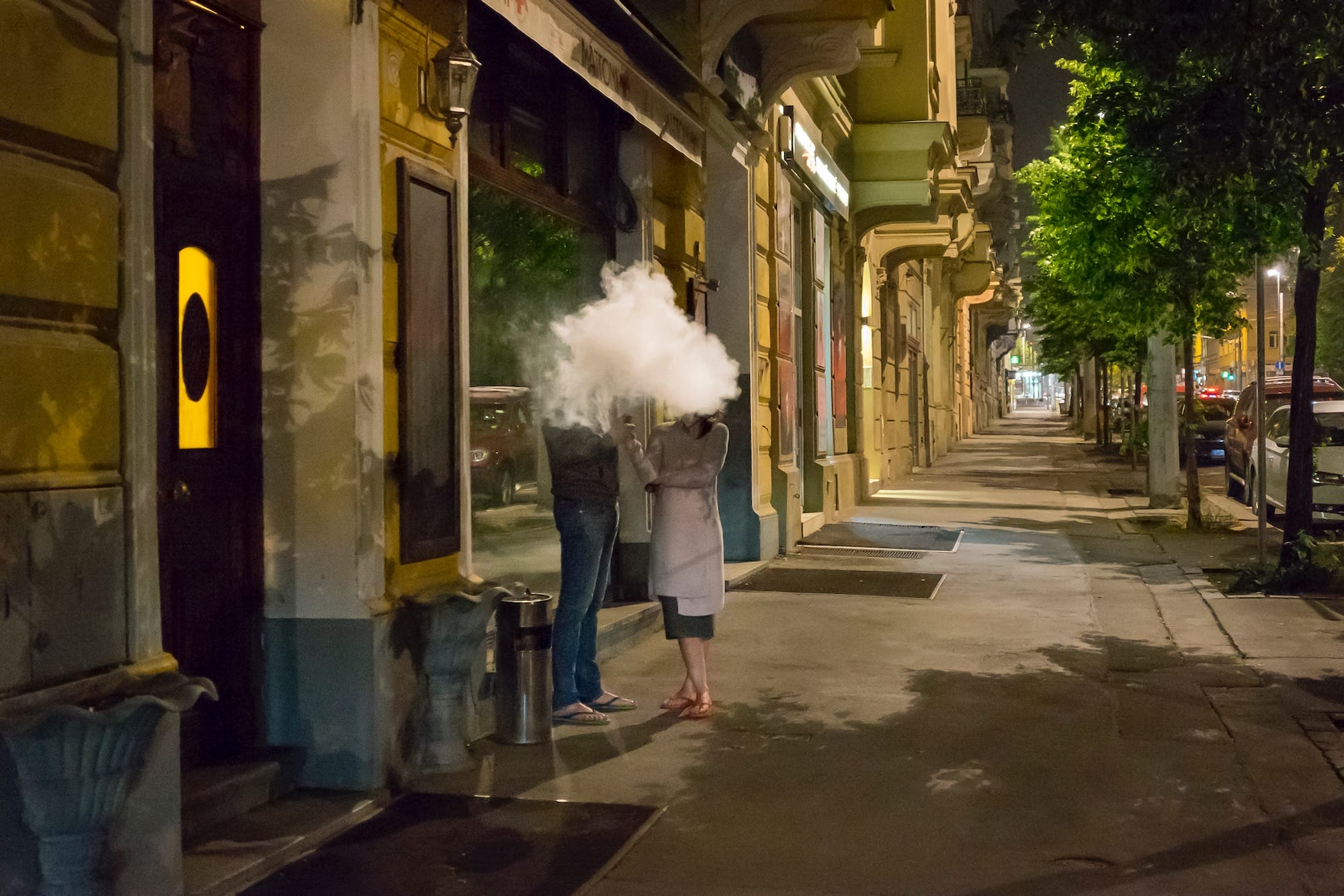 a photograph of two people standing outside on a street in a cloud of smoke