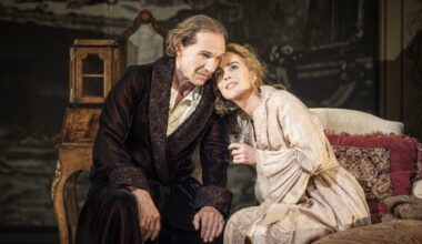 A woman in a pale robe leans against a man in a beaded velvet dressing gown