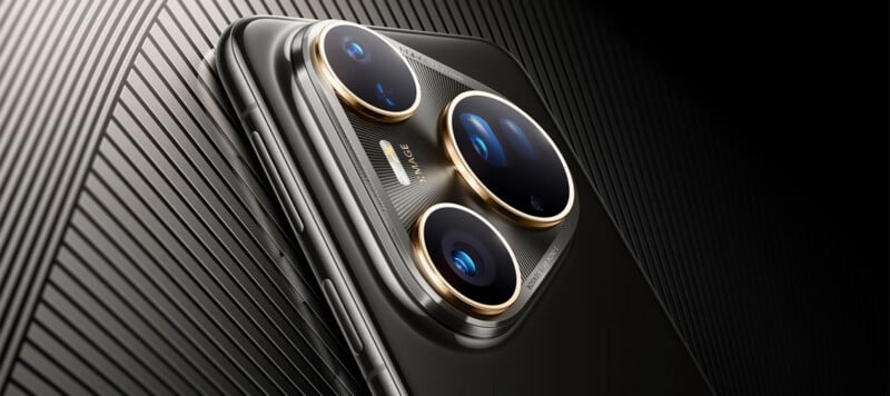 Close-up of the back of a sleek smartphone with three large camera lenses and gold accents, placed on a textured black surface with diagonal lines.