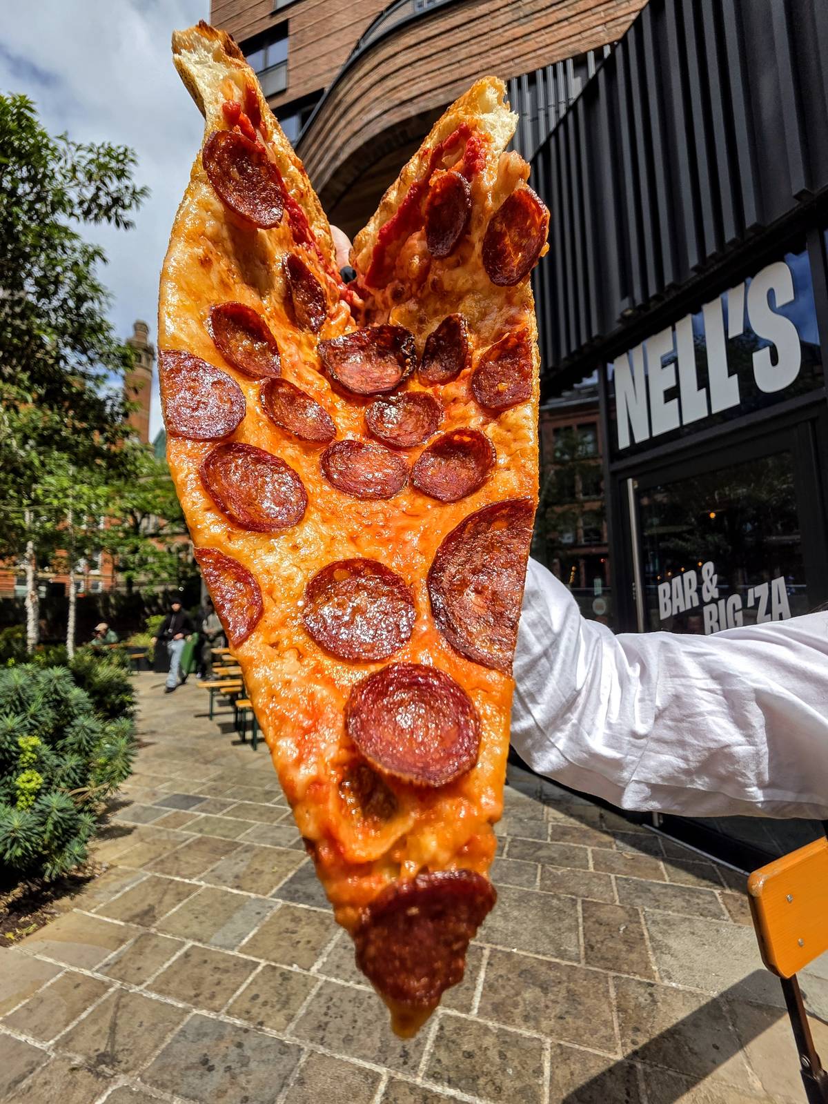 huge slice of pepperoni pizza held up outside nell's kampus in manchester