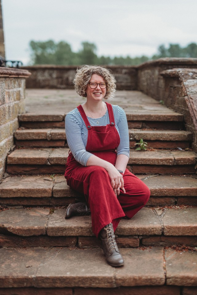 Woman in red overalls sitting on stone steps.