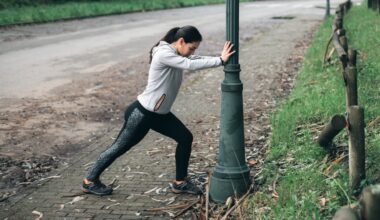 woman in leggings and hoodie doing a calf stretch against a lampost in a park setting