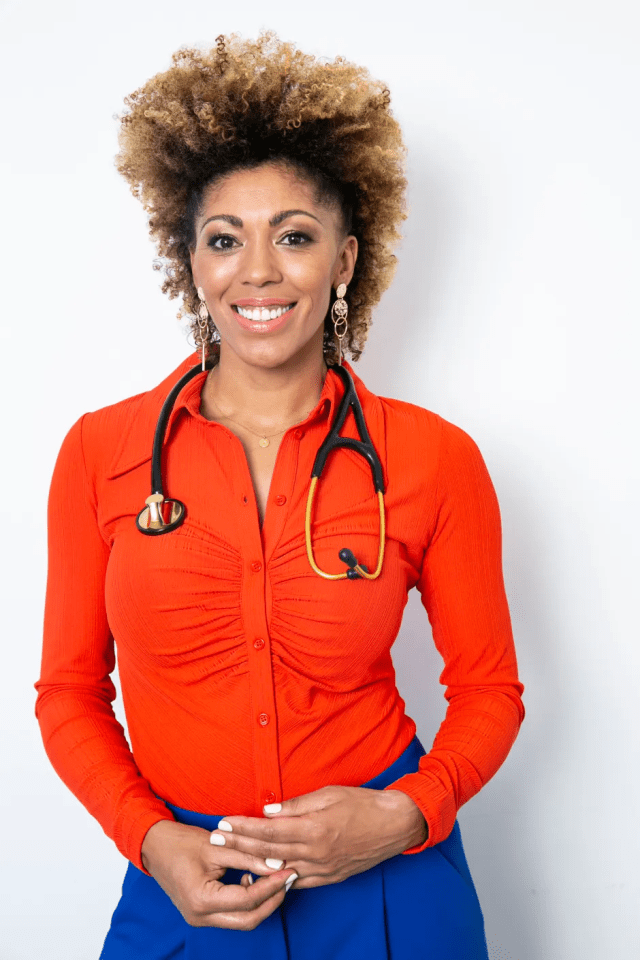 Portrait of a smiling woman doctor wearing a red shirt and blue pants.