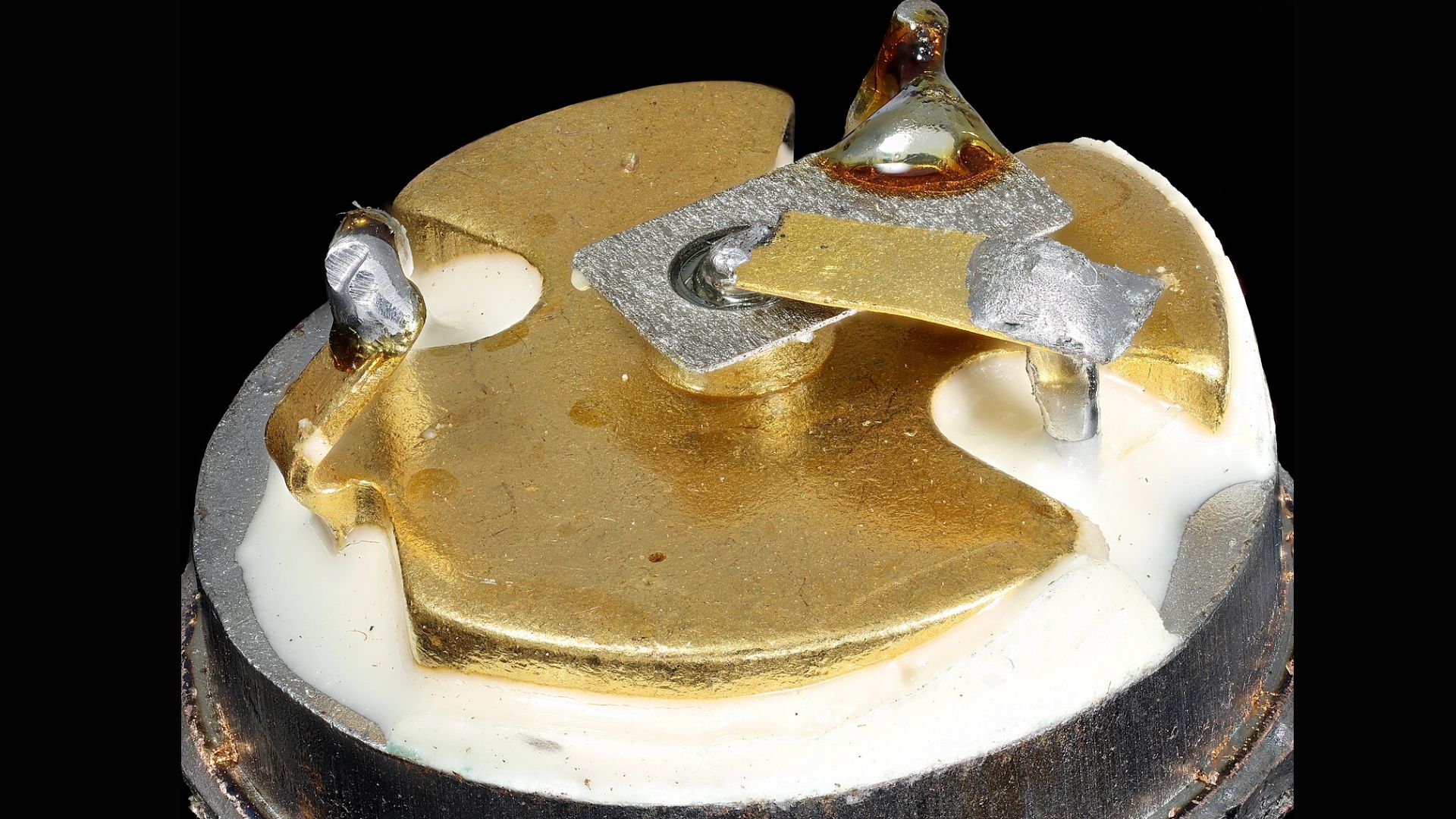 View of a transistor with gold circuits and wire bonds on ceramic substrate. 