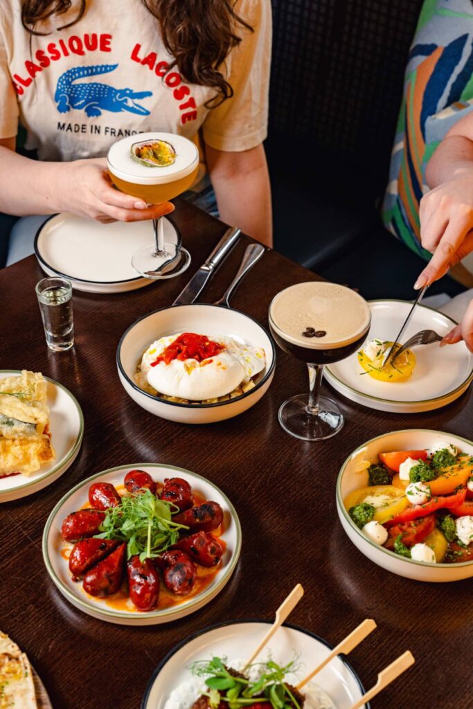 A vibrant spread of modern European small plates and cocktails at Burdock, a stylish restaurant from the ETM Collection. Food is placed tidily in stylish plates on a table, with a wave of colour and different culinary options arranged decadently.