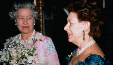 Queen Elizabeth wearing a patterned dress and holding flowers smiling at Princess Margaret