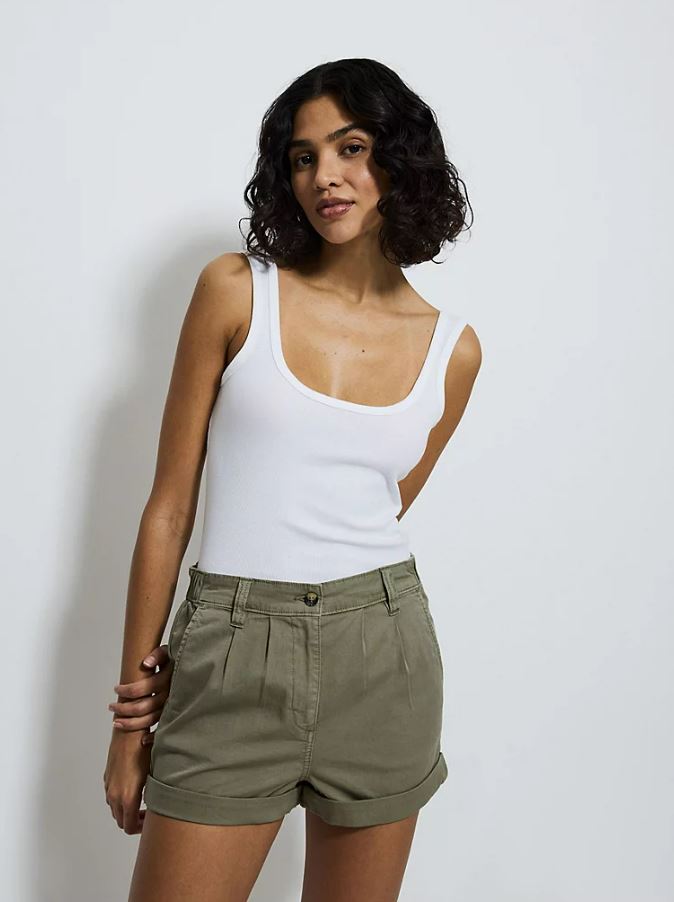 Woman wearing khaki shorts and a white tank top.