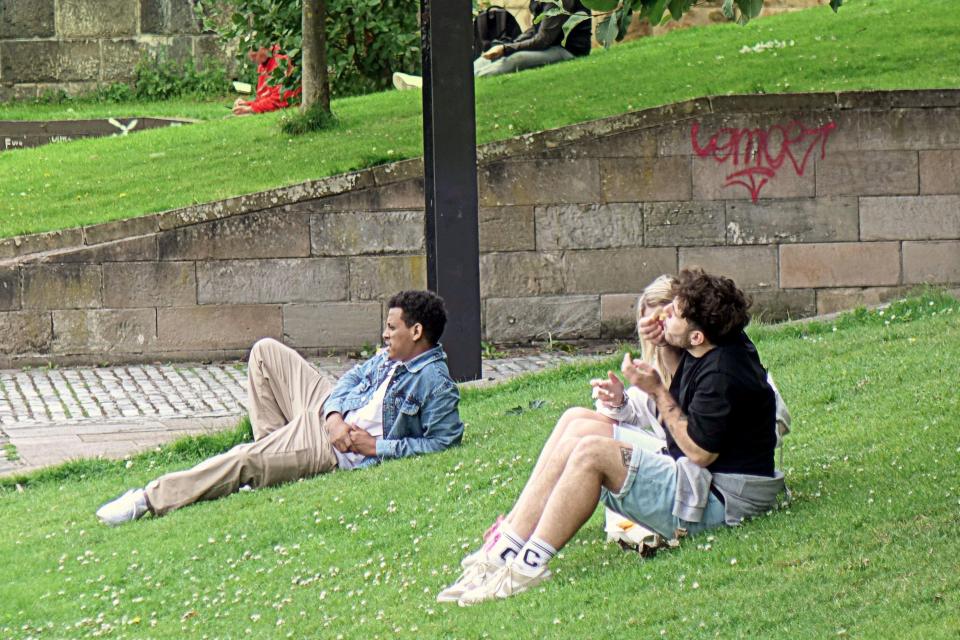 People relaxing on a grassy area next to a stone wall.