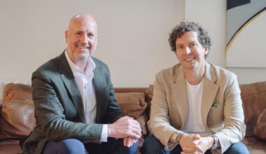 Two men sitting on a sofa smiling.