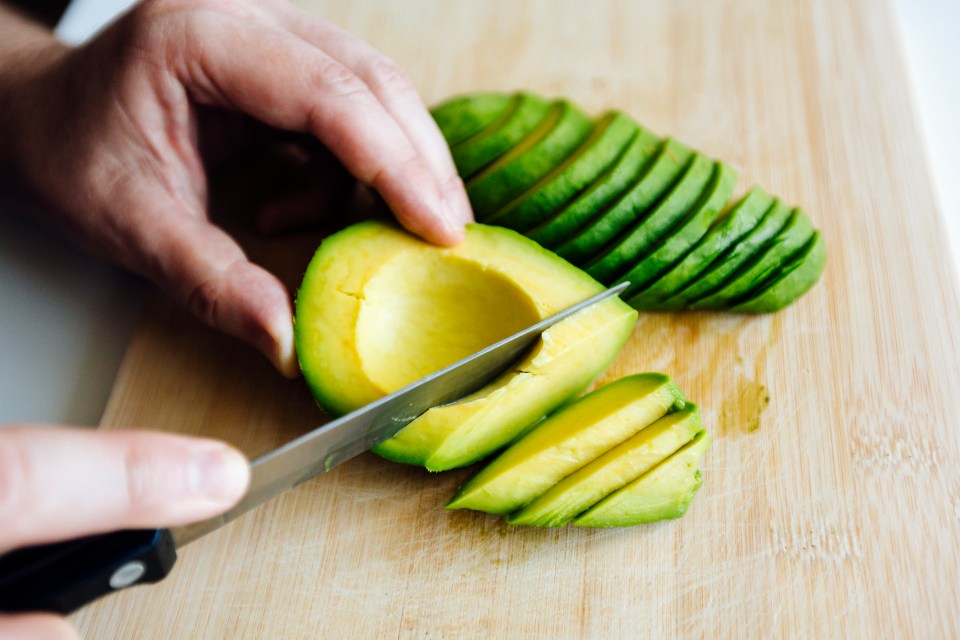 Person slicing an avocado on a wooden cutting board.