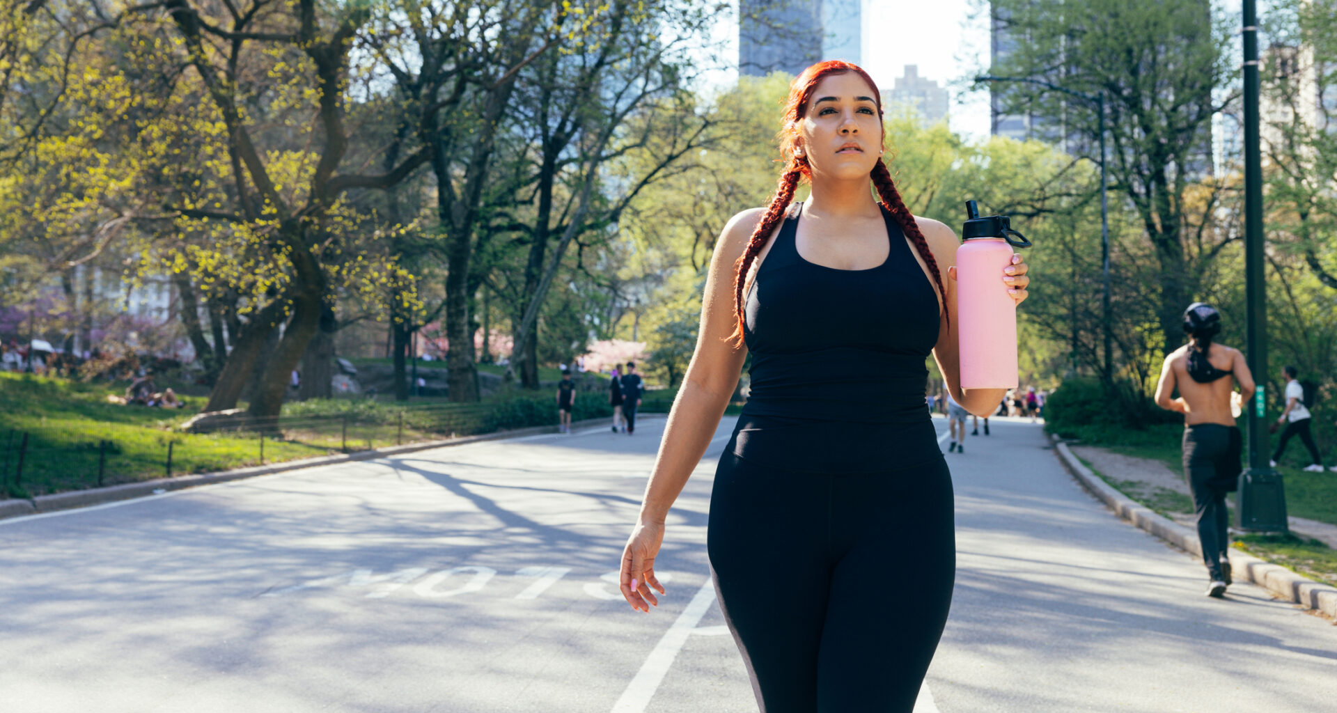 Woman walking in Central Park holding large pink water bottle