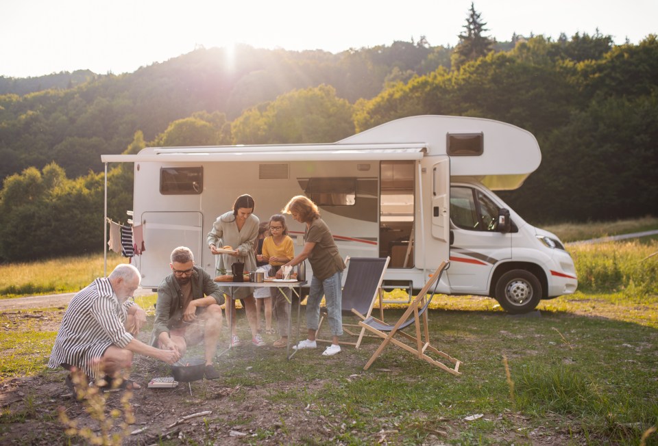 Multi-generational family cooking outdoors near a camper van.