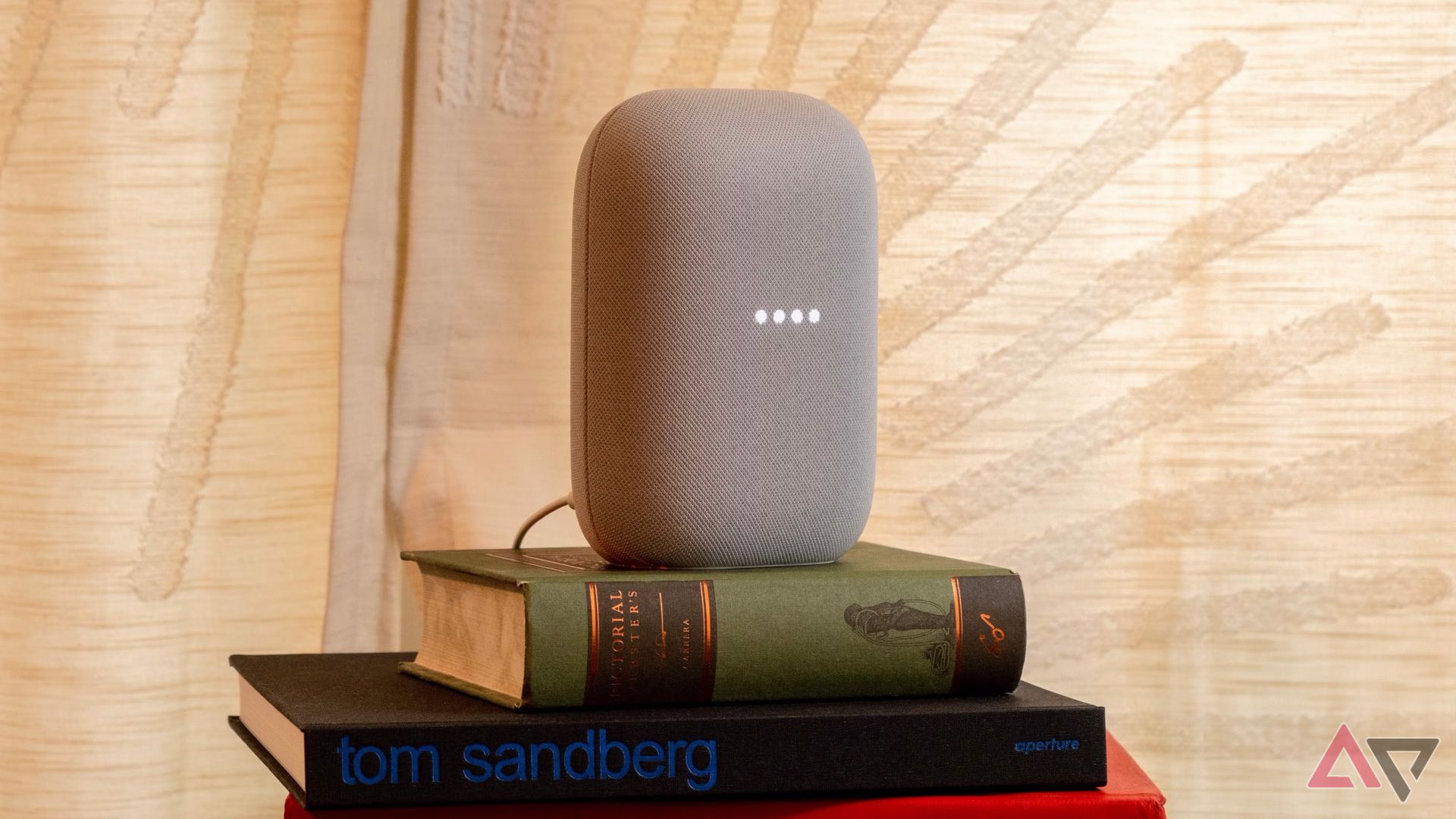 The Nest Audio speaker with its lights active, sitting on a small pile of books
