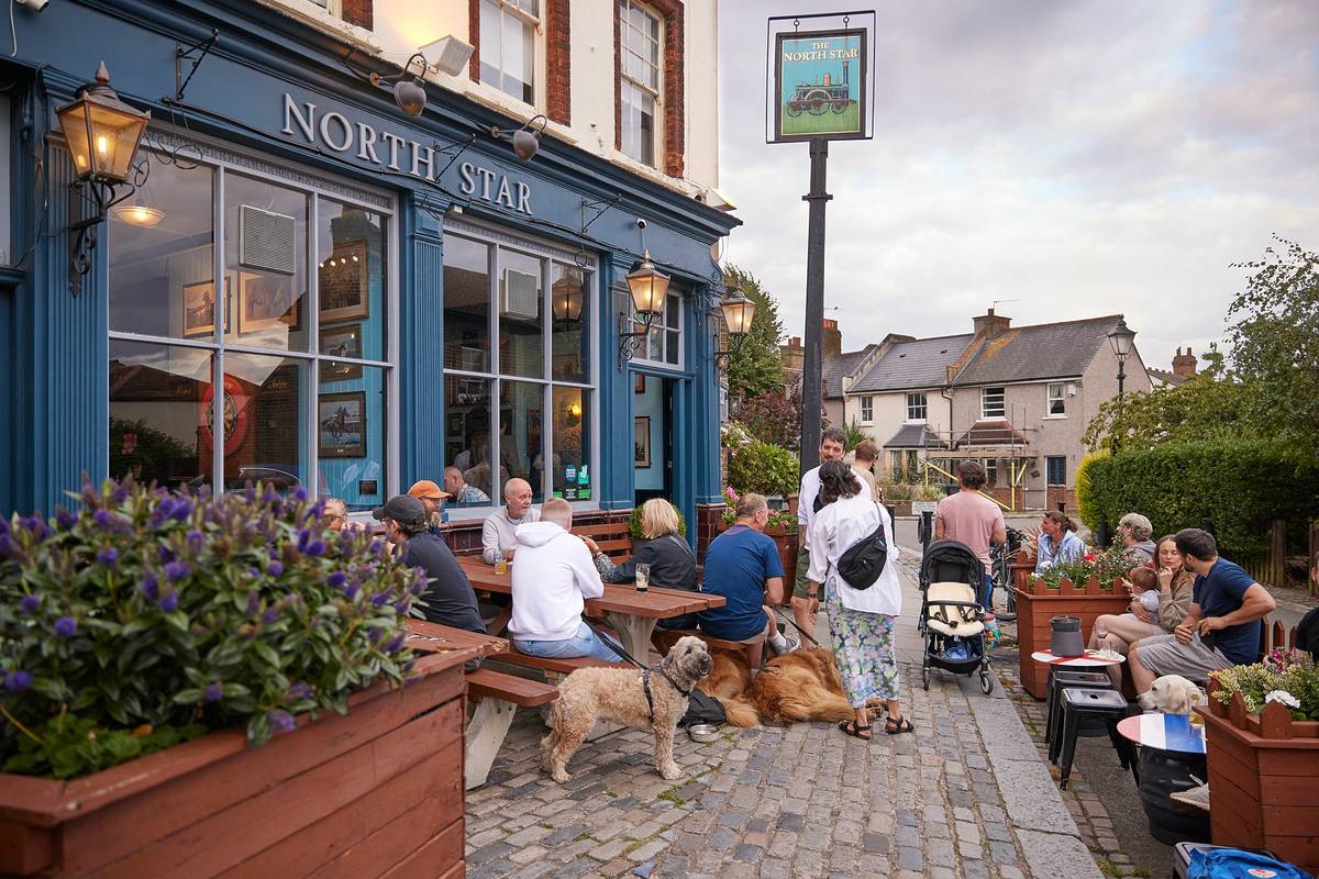 people and dogs sat around outdoor tables enjoying an afternoon at the pub