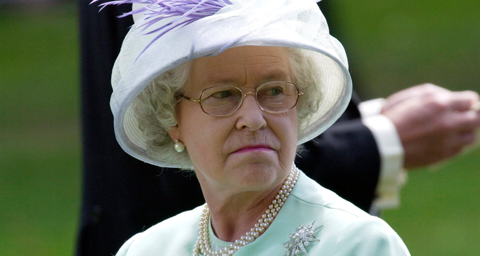 Queen Elizabeth wears a mint green suit and matching hat with a brooch and pearl necklace