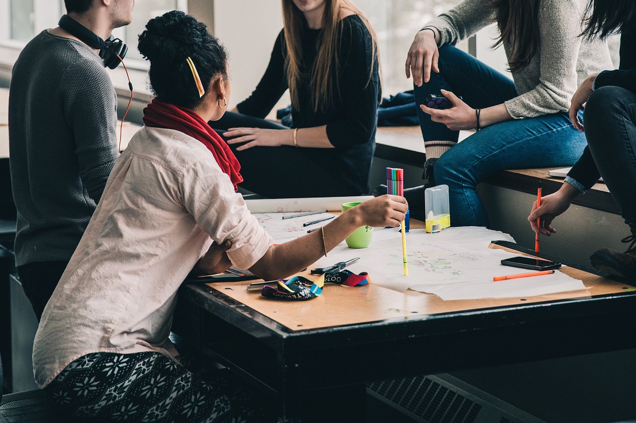 Group of young adults collaborating around a table with papers, pens, and colorful markers.