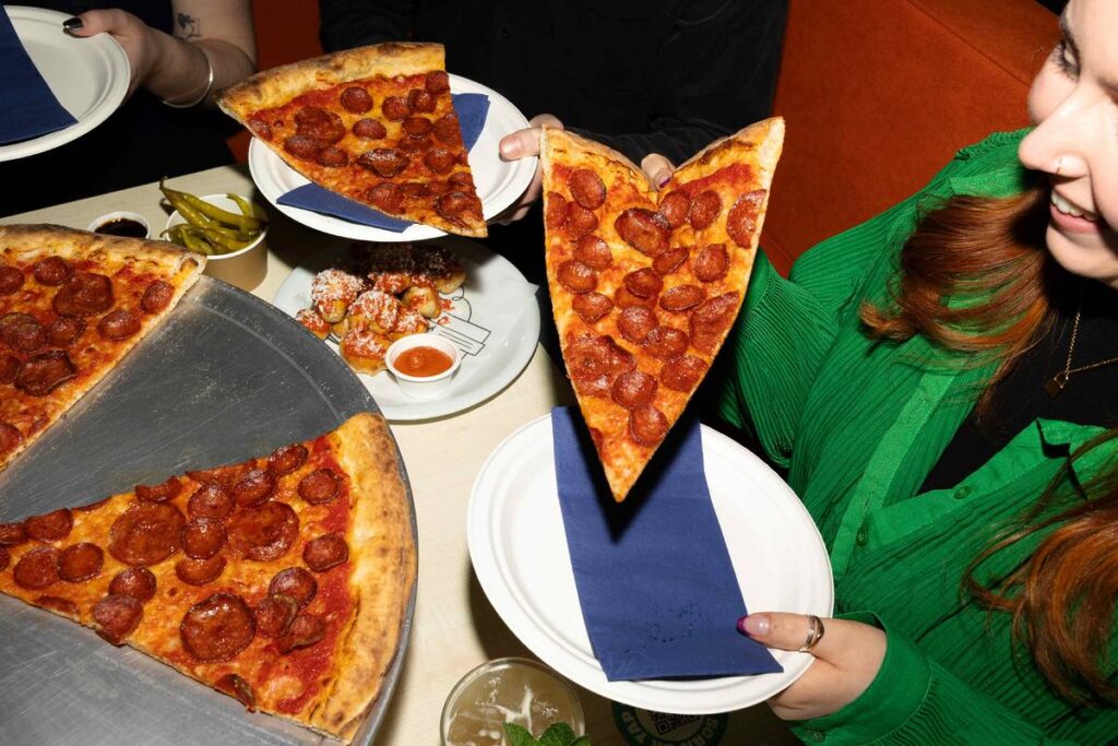 people eating slices of pepperoni pizza at nell's