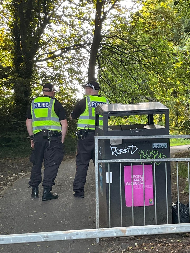 Two police officers standing by a trash can in a park.