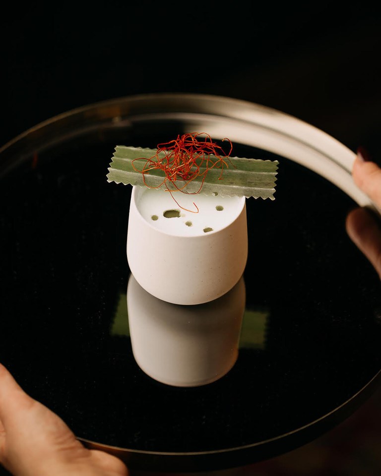 Small white cup with garnish on a black tray.