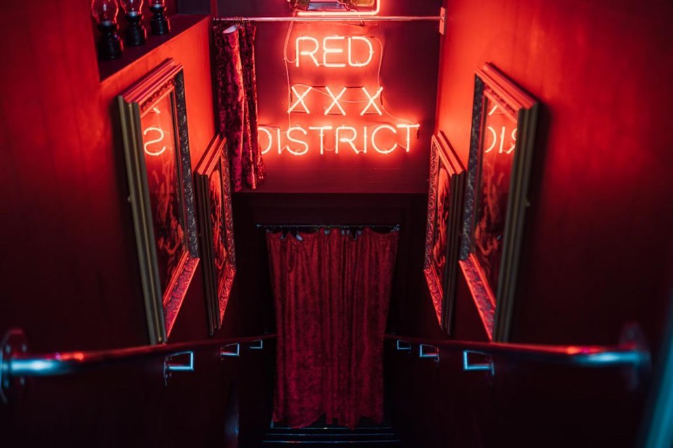 Neon sign reading "Red XXX District" above a staircase in a dimly lit room.