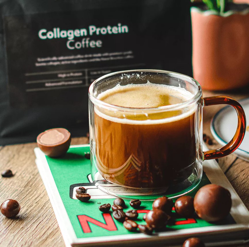 Collagen protein coffee in a glass mug with chocolates and coffee beans.