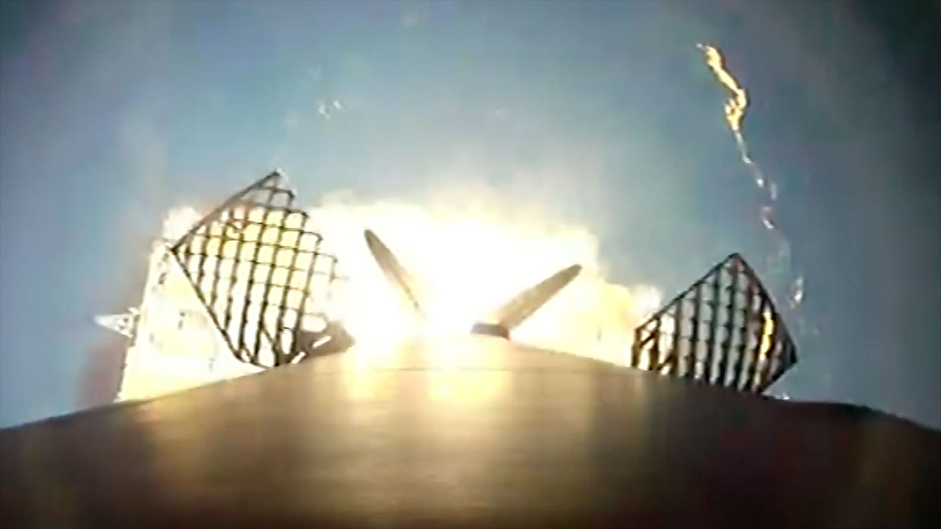 a downward facing camera mounted to the side of a rocket's first stage captures the view as it nears a propulsive landing on four deployed landing legs on an ocean-based droneship.