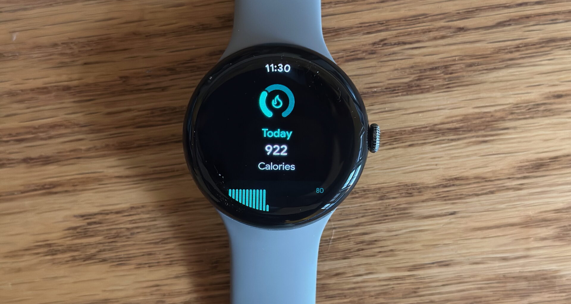 The Google Pixel Watch 3 sitting on a desk, showing a daily calorie count widget.